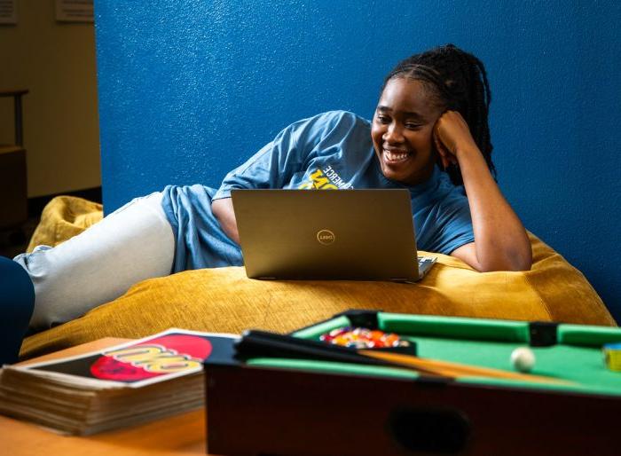 Girl lays on her side, propped up on her arm, as she looks at her laptop.